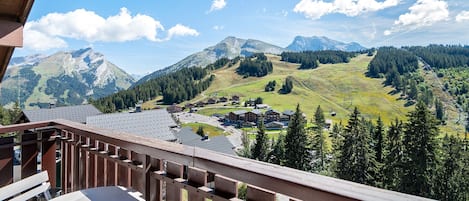A balcony with a view of a mountainous landscape, a wooden railing, and a table with a chair.