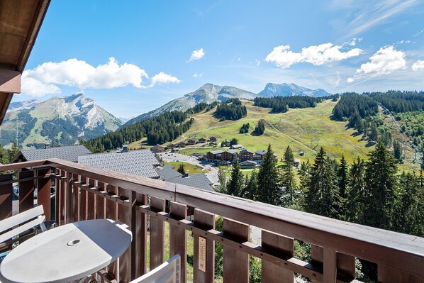 Ein Balkon mit Blick auf eine gebirgige Landschaft, einem Holgitter und einem Tisch mit einem Stuhl.