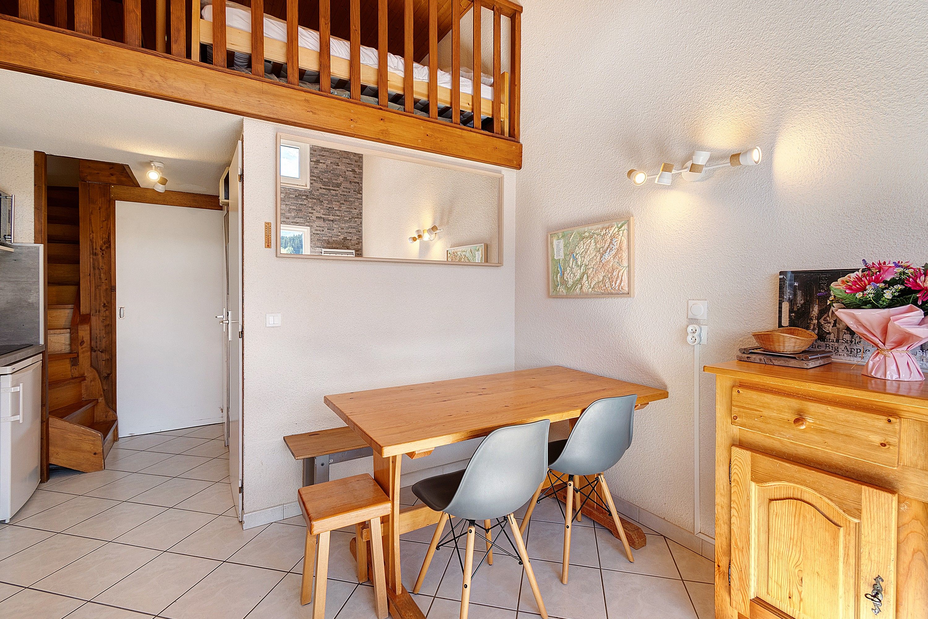 Un espace repas avec une table et des chaises en bois, un coin cuisine équipé d’une cuisinière, et un escalier menant à un niveau supérieur.