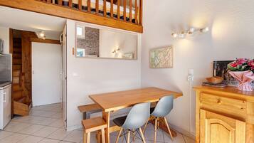 Un espace repas avec une table et des chaises en bois, un coin cuisine équipé d’une cuisinière, et un escalier menant à un niveau supérieur.