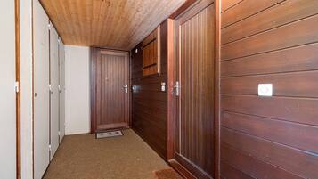 A narrow hallway with wooden walls and a wooden ceiling. There are doors on the left and a large wooden cabinet on the right.