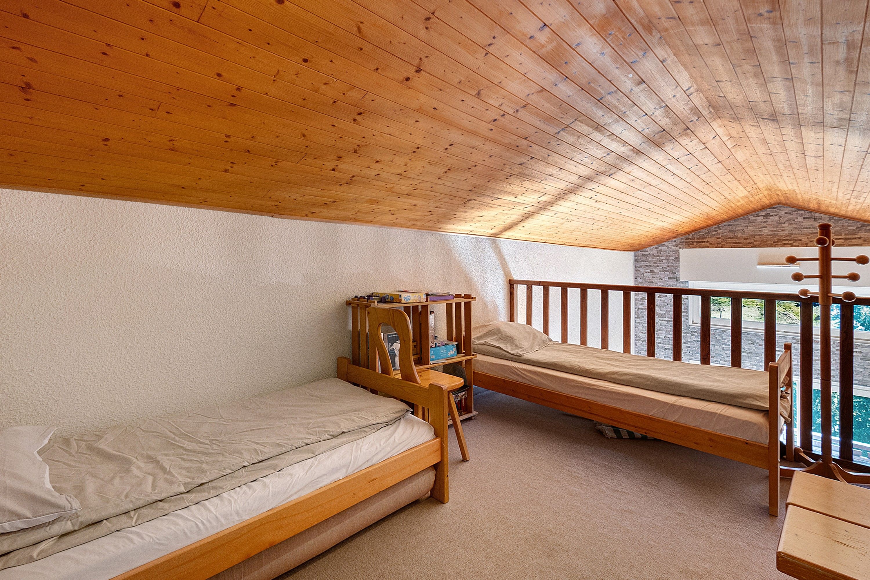 A room with two wooden bunk beds, a small desk, and a window overlooking a stone wall.