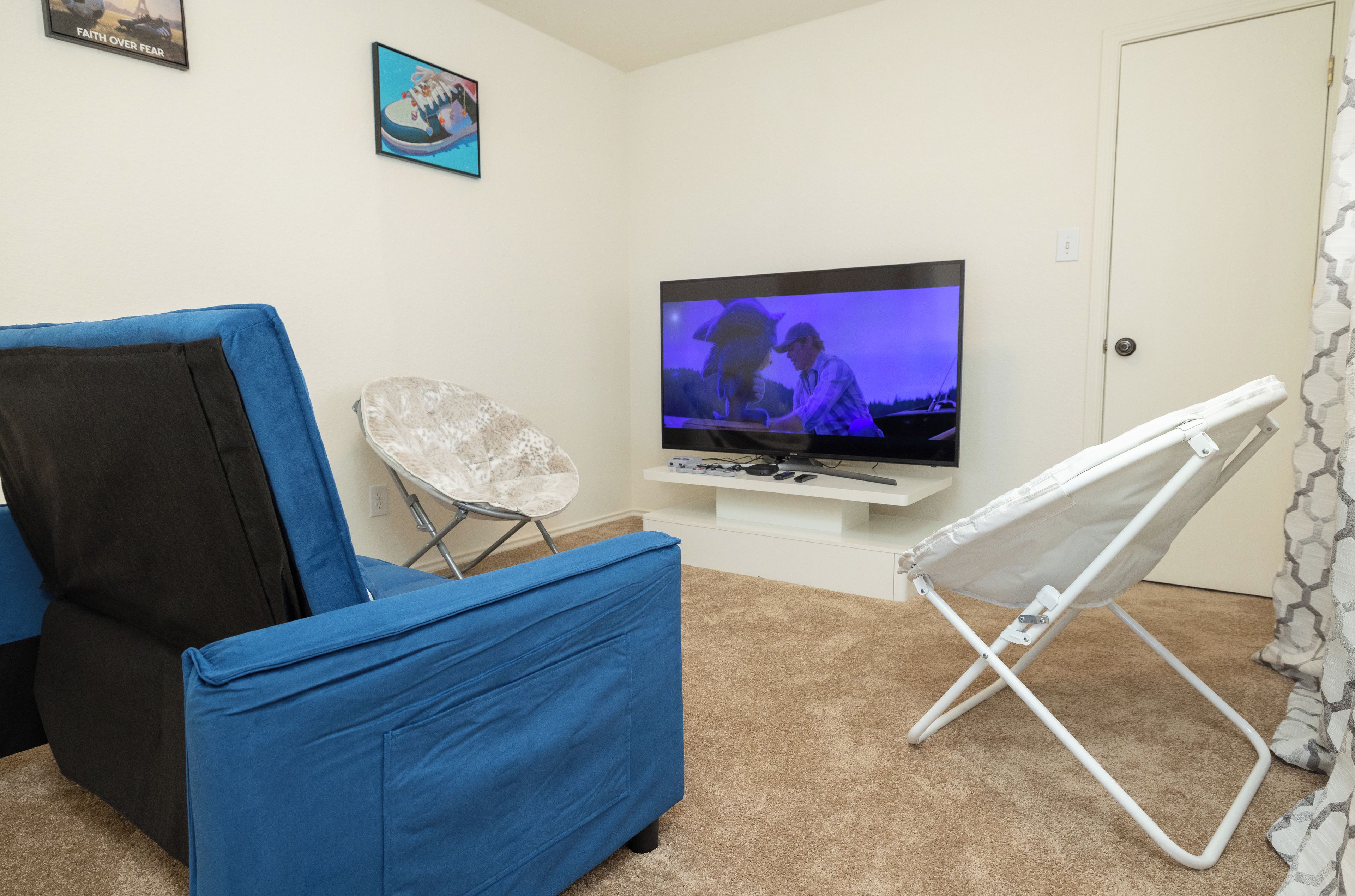 A living room with a television, a blue couch, a white folding chair, and a door.