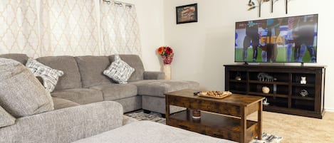 A living room with a sectional sofa, a coffee table, a flat-screen TV, and a decorative wall piece.