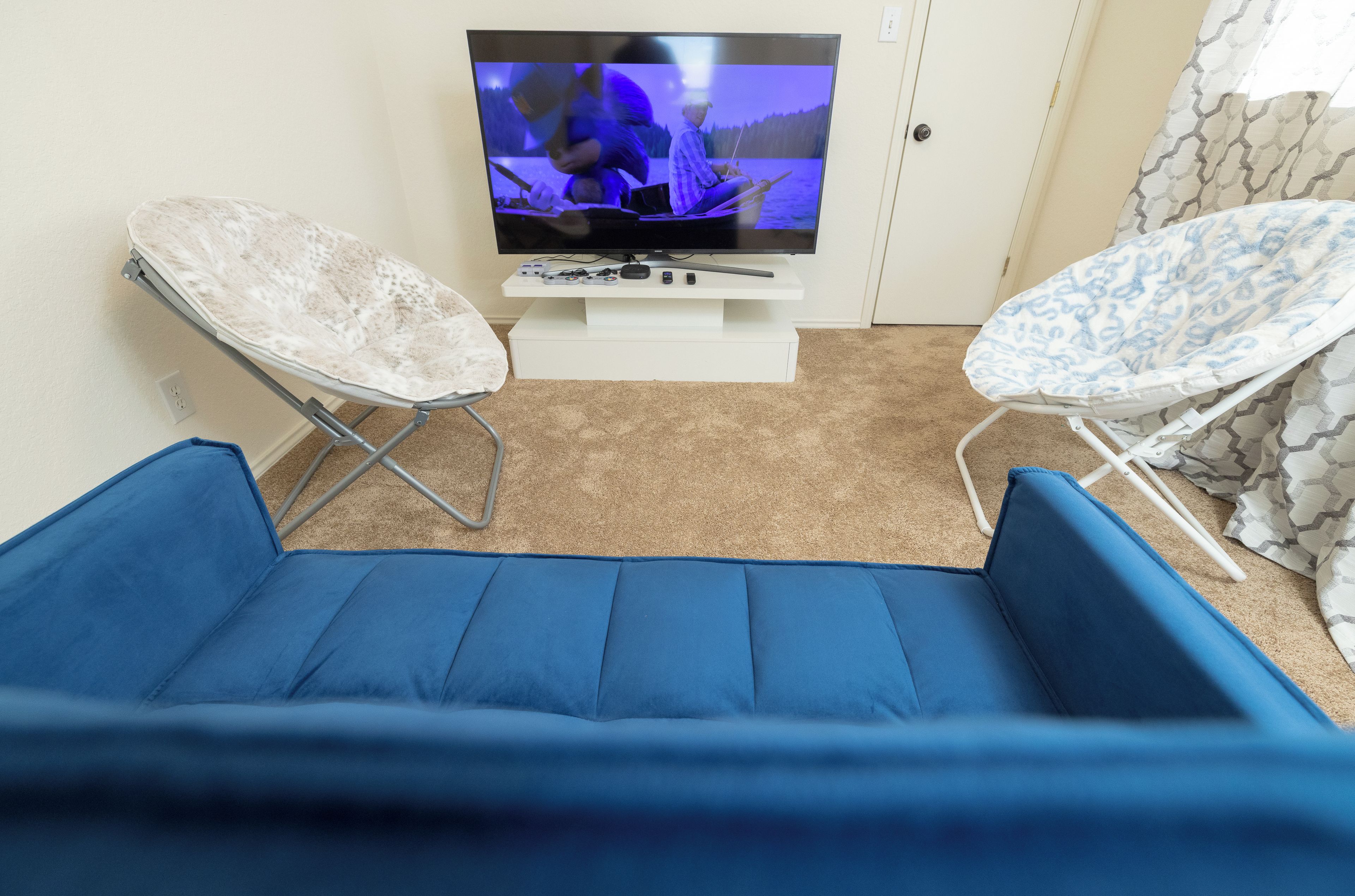 Une pièce avec un téléviseur posé sur un meuble, deux chaises pliantes et un espace agrémenté de coussins bleus.