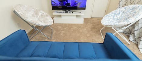 A room with a television on a stand, two foldable chairs, and a blue cushioned area.