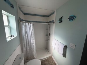 Et badeværelse med brusebad, toilet, vask og et vindue.