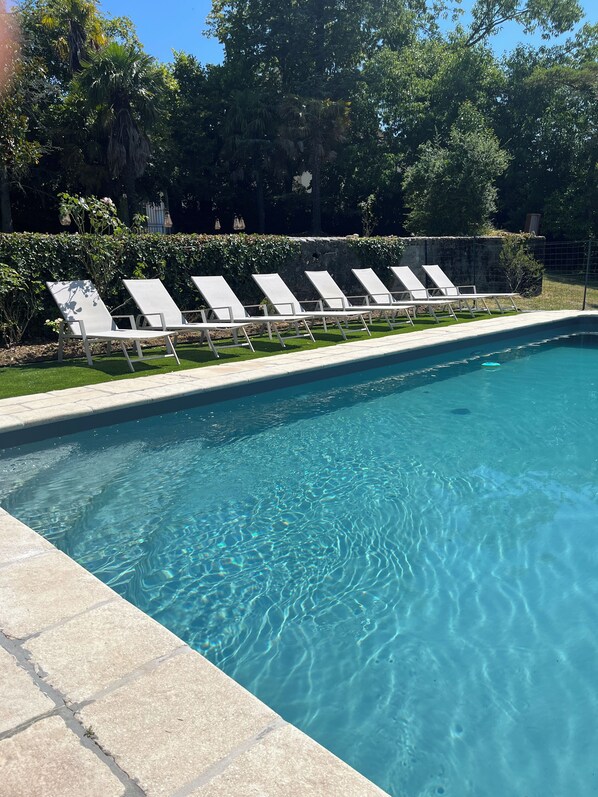 A swimming pool with clear blue water, surrounded by a tiled deck and white lounge chairs.