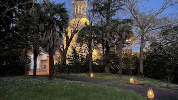 Un chemin menant à un bâtiment doté d’une tour, entouré d’arbres et illuminé par des lanternes suspendues.