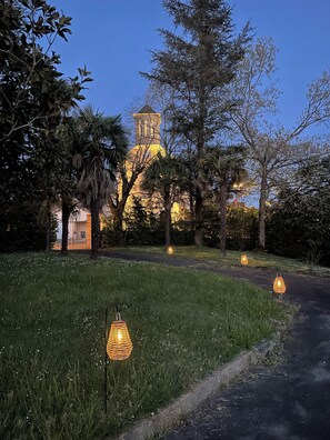 A pathway leading to a building with a tower, surrounded by trees and illuminated by hanging lanterns. - Beautiful family holiday château with stunning views and private pool. (Serres-Sainte-Marie)