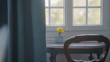 A room with a window, a table with a vase of flowers, and a chair.