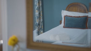 Een net opgemaakt bed met witte lakens en twee kussens, waarvan er één een blauwe hoes heeft en de ander een bruine rand.