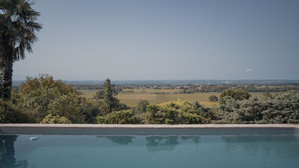 A pool with a view of a rural landscape, including fields and distant buildings.