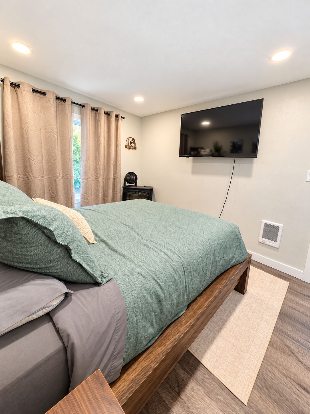 A bedroom with a bed, a television mounted on the wall, and a small table with a fan.
