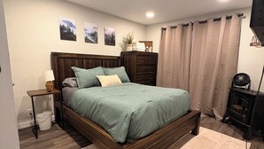 Ein Schlafzimmer mit einem hölzernen Bett, einem Nachttisch, einer Lampe, einer Wandheizung und einem Fenster mit Vorhängen.