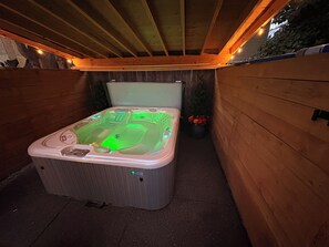 Un jacuzzi rodeado por una terraza de madera, una planta en maceta y una pared de piedra.