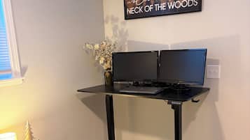 Un espacio de trabajo en casa con un escritorio, dos monitores, una computadora portátil, una planta pequeña y un letrero decorativo en la pared.