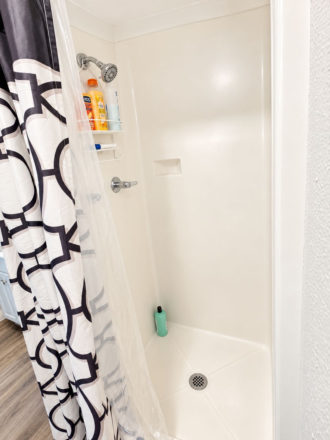 A shower area with a white bathtub, a showerhead, and a shelf with toiletries.