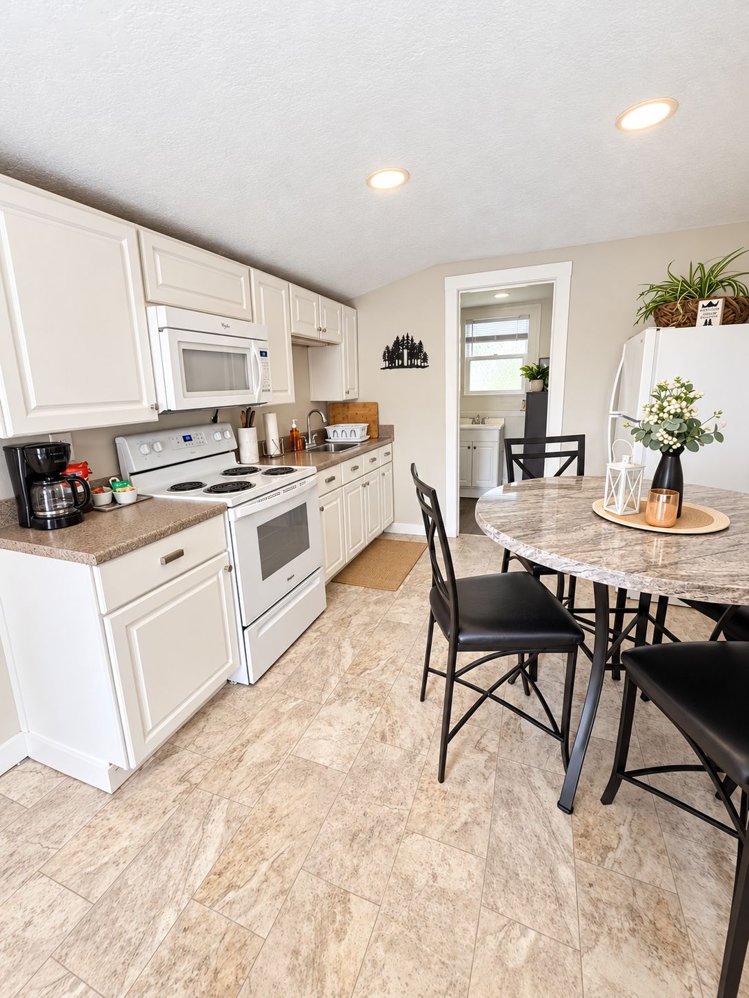 A modern kitchen with white cabinetry, a built-in oven, and a dining area with a round table and black chairs.