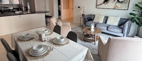 Un salon moderne avec un canapé gris, une table basse et un coin repas avec une table dressée pour quatre personnes.