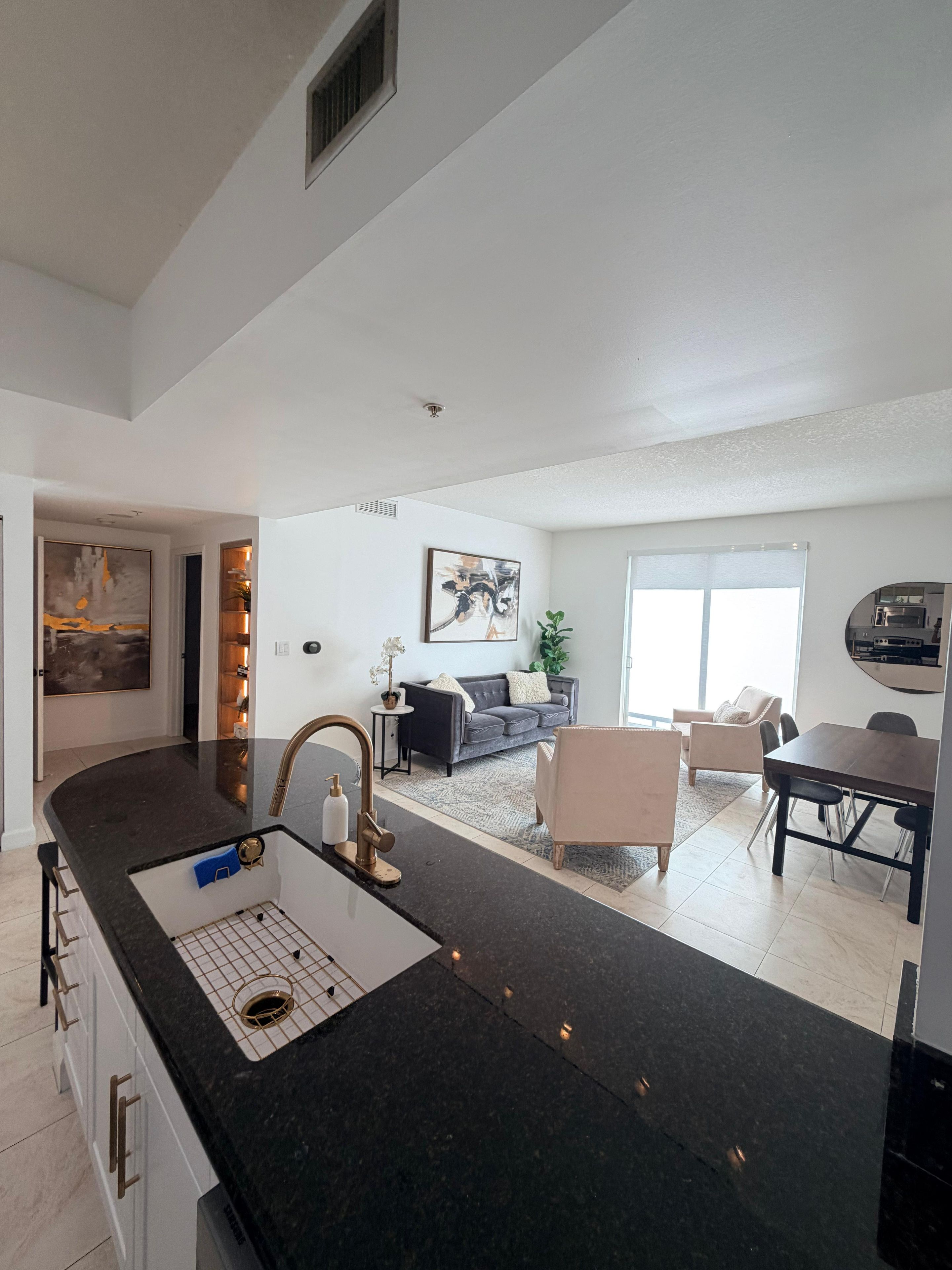 A modern kitchen with a black countertop, a sink, and a dining area with a table and chairs.
