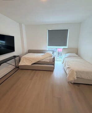 Una habitación con dos camas, una televisión de pantalla plana y una ventana con vistas a un edificio.