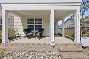 A covered porch with two chairs, a brick pathway, and a sign indicating short-term rental property. - Brand New 4BR | 2 Blks to Beach & Atlantic Park (Virginia Beach)