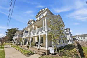 A two-story residential building with a covered porch and a small garden area. - Brand New 4BR | 2 Blks to Beach & Atlantic Park (Virginia Beach)