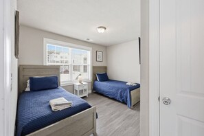 A bedroom with two beds, a nightstand, a window with blinds, and a door. - Brand New 4BR | 2 Blks to Beach & Atlantic Park (Virginia Beach)