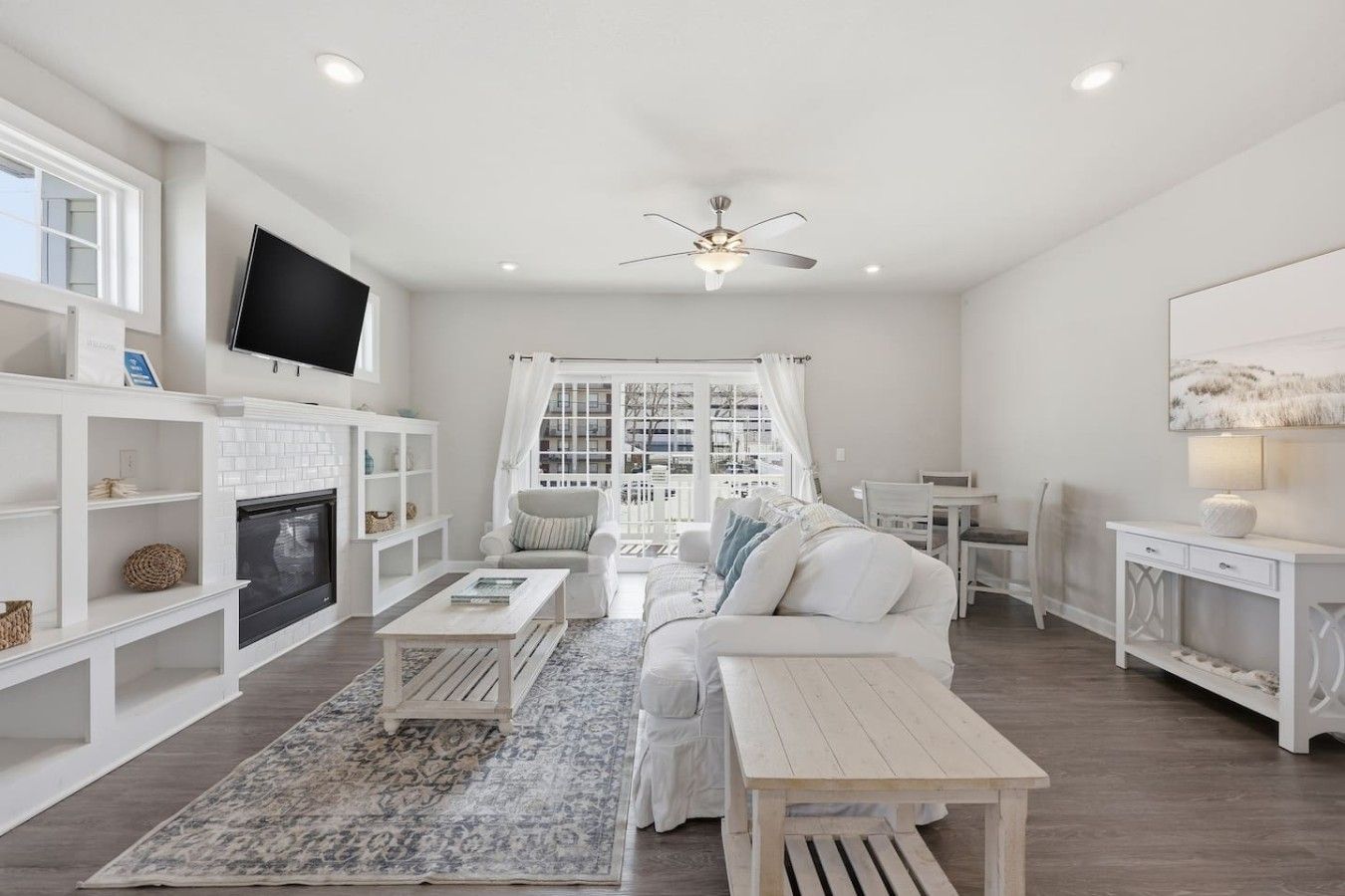 A modern living room with a fireplace, white furniture, and a large window with curtains.