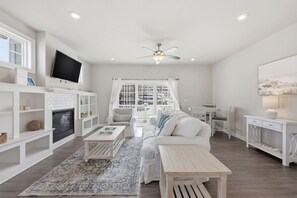 A modern living room with a fireplace, white furniture, and a large window with curtains. - Brand New 4BR | 2 Blks to Beach & Atlantic Park (Virginia Beach)