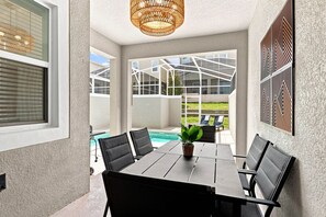 A dining area with a table and chairs, a hanging light fixture, and a view of a swimming pool. - Themed Family Getaway, Private Pool, Top Location (Four Corners)