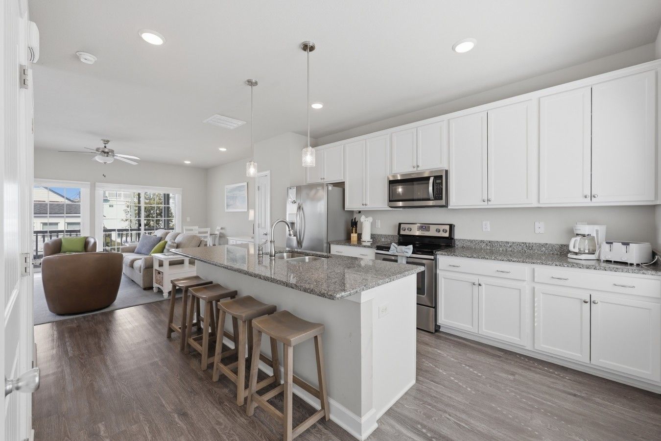 A modern kitchen with white cabinetry, a granite countertop, stainless steel appliances, and a bar stool area.