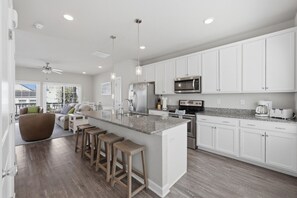 A modern kitchen with white cabinetry, a granite countertop, stainless steel appliances, and a bar stool area. - VIBE 3BR | 2 Blks to Beach & 1 blck Atlantic Park (Virginia Beach)