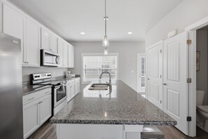 A modern kitchen with white cabinetry, a granite countertop, a stainless steel refrigerator, and a built-in microwave. - VIBE 3BR | 2 Blks to Beach & 1 blck Atlantic Park (Virginia Beach)