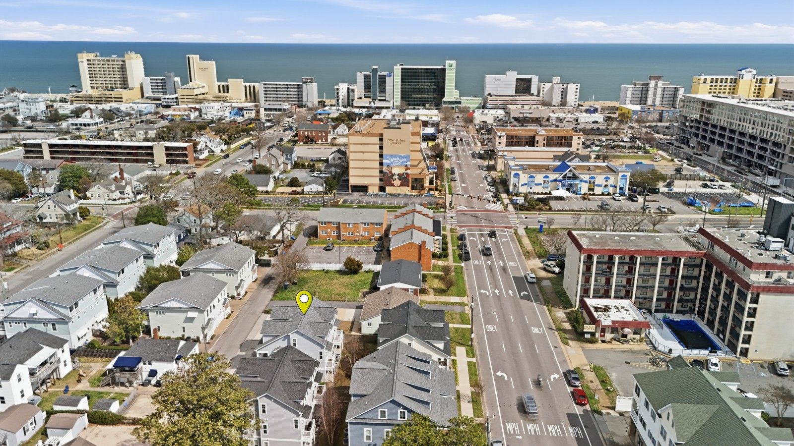 An aerial view of a coastal city with a mix of residential and commercial buildings, a prominent highway, and a view of the ocean.