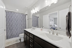 Une salle de bain avec un double lavabo, un miroir et un rideau de douche.