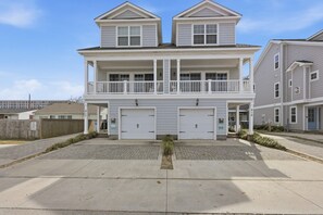 A two-story residential building with a balcony, two garages, and a paved driveway. - VIBE 3BR | 2 Blks to Beach & 1 blck Atlantic Park (Virginia Beach)
