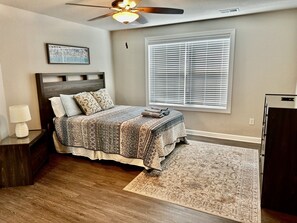 A bedroom with a bed, a nightstand, a lamp, a ceiling fan, a window with blinds, and a rug. - Brand New 4BR | 2 Blks to Beach & Atlantic Park (Virginia Beach)