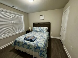 Une chambre à coucher avec un lit, une table de chevet, une fenêtre avec des stores et une porte.