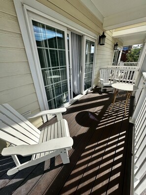 Eine überdachte Terrasse im Freien mit weißen Adirondack-Stühlen und einem kleinen runden Tisch.