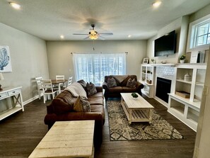 A living room with a sofa set, coffee table, TV, fireplace, and a view of the city. - Brand New 4BR | 2 Blks to Beach & Atlantic Park (Virginia Beach)