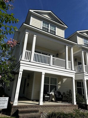 A two-story residential building with a balcony, a porch with outdoor furniture, and a brick foundation. - Brand New 4BR | 2 Blks to Beach & Atlantic Park (Virginia Beach)