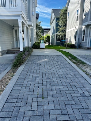 Una calle residencial con sendero pavimentado, casas y un letrero que indica una propiedad de alquiler a corto plazo.