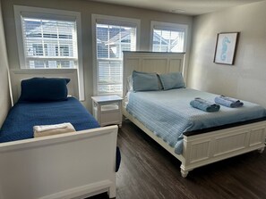A bedroom with two beds, one with a blue bedspread and the other with a light blue bedspread. There is a small bedside table with a lamp, and a framed picture on the wall. - Coastal 3BR | 2 Blks to Beach & Atlantic Park (Virginia Beach)