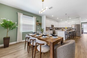 A modern kitchen with white cabinets, stainless steel appliances, and a central island with bar stools. - Brand New   Family 6BR Pool Spa   Game Lounge 7875 (Kissimmee)