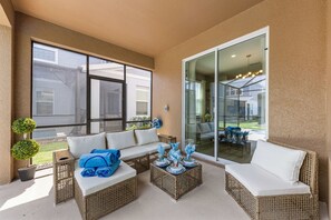 A sunlit outdoor seating area with wicker furniture, a glass door leading to a patio, and a view of a residential neighborhood. - Brand New   Family 6BR Pool Spa   Game Lounge 7875 (Kissimmee)
