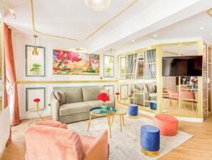 Ein modernes Wohnzimmer mit einer Couch, einem Couchtisch, einem Hocker, einem Fernseher und einem Bild an der Wand.