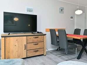 A modern dining area with a wooden table, black chairs, a television on a wooden cabinet, and a pendant light. - 4.3/t2 Holiday Park "freesenbruch" (Zingst)