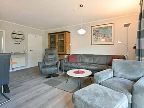 A modern living room with a grey sofa, a grey armchair, a small round table, and a cabinet with glass doors. - 4.3/t2 Holiday Park "freesenbruch" (Zingst)
